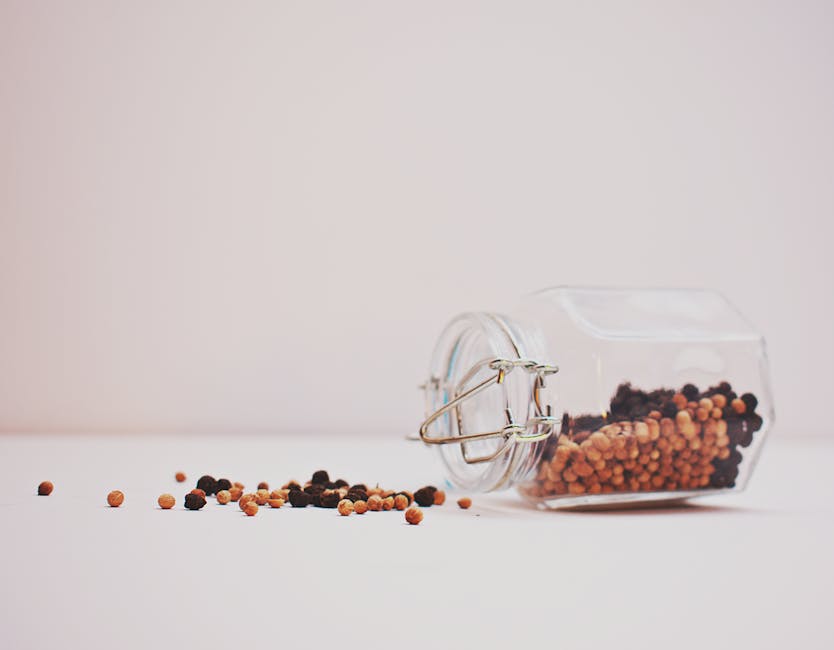 A glass jar tipped over with colorful peppercorns on a minimalist white background.